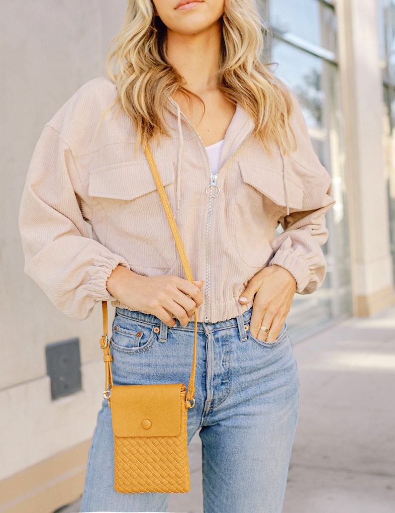 May include: A woman wearing a light beige corduroy jacket with a zipper and a yellow woven crossbody bag. The bag has a flap with a button closure.
