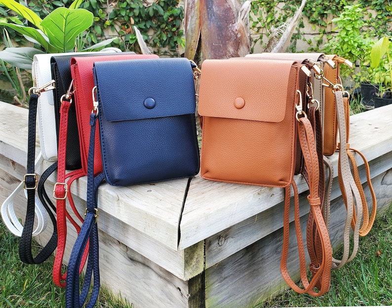 Puede incluir: Cinco bolsos de bandolera de cuero de diferentes colores con correas ajustables. Los bolsos est&aacute;n dispuestos en fila sobre una superficie de madera. Los bolsos son todos del mismo tama&ntilde;o y forma, pero son de diferentes colores: blanco, rojo, azul, marr&oacute;n y beige.