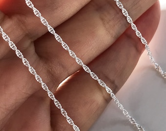 May include: Three silver rope chains of varying lengths, displayed on a hand.