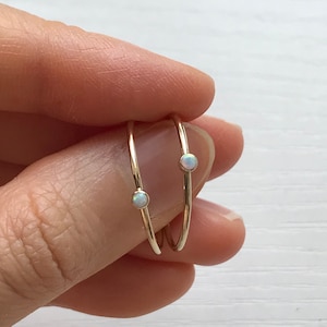 Könnte beinhalten: Zwei zarte goldene Ringe mit kleinen weißen Opal-Steinen. Die Ringe sind auf einem Finger übereinander gelegt.