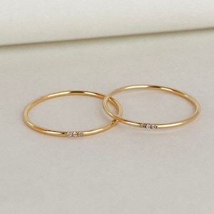 May include: Two thin gold rings with a row of three small diamonds on one ring.