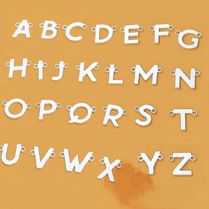 May include: Silver alphabet charms, each with a loop for attaching to jewellery or other crafts. The letters A to Z are displayed against a solid orange background. These charms are ideal for personalised necklaces or bracelets.