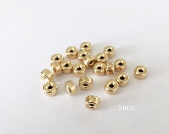 May include: A pile of 20 gold-colored metal beads, each measuring 5 mm in diameter. The beads are round with a hole in the center.