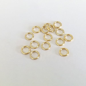 May include: A group of 15 gold jump rings, a type of jewellery finding, scattered on a white surface.