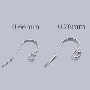 May include: Two silver earring hooks. One hook is labelled 0.66mm, the other is labelled 0.76mm. The hooks have a curved design with a small ball at the end of the curved section. The background is a light grey colour.