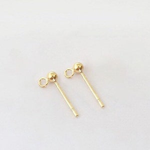 May include: Two gold-toned earring posts with a small ball at the top and a loop at the bottom.