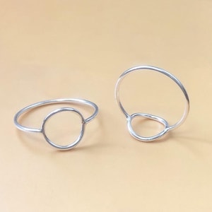 Könnte beinhalten: Zwei silberne Ringe mit einem Kreisdesign. Ein Ring hat einen durchgehenden Kreis, während der andere einen Kreis mit einer Lücke oben hat.