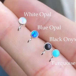 May include: Close-up of four small, round earrings in white opal, blue opal, black onyx, and turquoise. Each earring has a silver-colored setting and a small loop. The text in the image reads "White Opal", "Blue Opal", "Black Onyx", and "Turquoise".