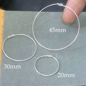Könnte beinhalten: Drei silberne Creolen in verschiedenen Größen. Die größte Creole hat einen Durchmesser von 45 mm, die mittlere Creole einen Durchmesser von 30 mm und die kleinste Creole einen Durchmesser von 20 mm.