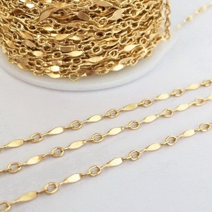 Könnte beinhalten: Goldkette mit flachem, ovalförmigem Glied. Die Kette ist um eine Spule gewickelt und in drei geraden Linien ausgelegt.