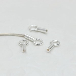 May include: Four silver-toned metal bead caps with a small loop at the top and a hollow tube at the bottom. The caps are designed to be used for attaching jewellery findings or other embellishments.