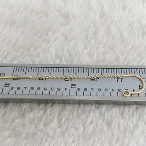 May include: A gold chain earring with a straight, thin bar and a curved hook. The earring is measured against a ruler, showing it is approximately 2 inches long.