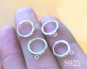 May include: Four silver hoop earring blanks with jump rings. The earring blanks are on a hand.