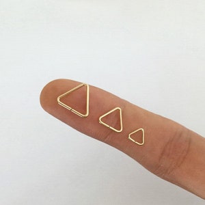 May include: Three gold triangle hoop earrings of different sizes. The earrings are shown on a finger.