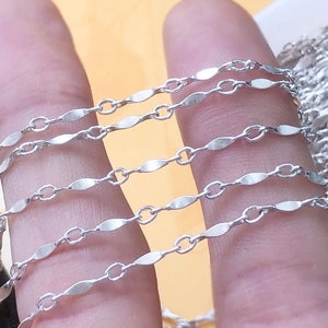 Könnte beinhalten: Nahaufnahme einer silbernen Kette mit einem flachen, ovalen Glied. Die Kette wird in mehreren Lagen gezeigt, wodurch das zarte Design hervorgehoben wird.