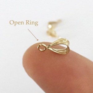 May include: Gold-toned open ring pendant bail with a smooth, slightly textured surface. The ring is open and ready to be attached to a chain or cord.