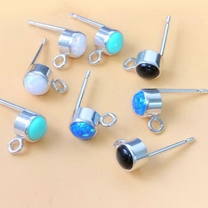 May include: Assortment of eight earring findings with different colored stones. The findings are silver-toned and have a loop at the top. The stones are turquoise, white opal, black onyx, and blue opal.
