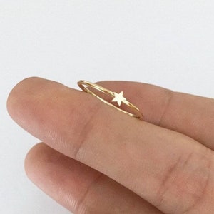 May include: A delicate gold ring with a small star charm. The ring is thin and simple, making it a perfect everyday accessory.