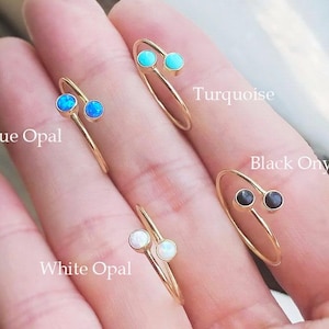 Puede incluir: Anillos dorados con varias opciones de piedras preciosas: ópalo azul, turquesa, ópalo blanco y ónix negro. Cada anillo presenta un diseño minimalista con dos piedras sobre una banda delgada. El texto etiqueta cada tipo de gema.