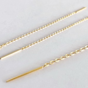 Pode incluir: Dois pares de extensões de brincos de ouro. Cada extensão é uma fina corrente de ouro com uma pequena barra de ouro na ponta.