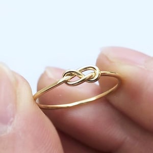 Op de afbeelding: Een gouden knoop ring met een eenvoudig ontwerp. De ring is gemaakt van dun draad en is een delicaat sieraad.