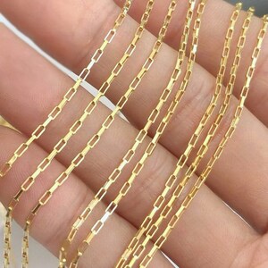 May include: Multiple gold chains with a box link pattern. The chains are laid out in a fan shape on a hand.