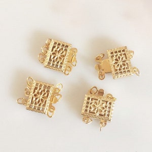 May include: Four gold-toned metal clasps with intricate floral designs. Each clasp has three loops for attaching jewelry.