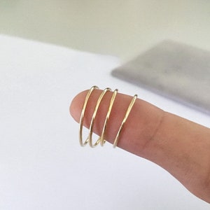 K&ouml;nnte beinhalten: F&uuml;nf d&uuml;nne, goldfarbene Ringe sind auf einem Finger gestapelt. Die Ringe sind schlicht und minimalistisch gestaltet und haben eine glatte, polierte Oberfl&auml;che. Die Ringe scheinen aus Metall zu sein und haben eine warme, gelbe Farbe.