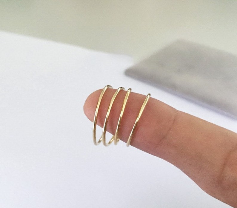 K&ouml;nnte beinhalten: F&uuml;nf d&uuml;nne, goldfarbene Ringe sind auf einem Finger gestapelt. Die Ringe sind schlicht und minimalistisch gestaltet und haben eine glatte, polierte Oberfl&auml;che. Die Ringe scheinen aus Metall zu sein und haben eine warme, gelbe Farbe.