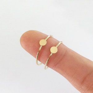 May include: Two gold rings with a small round disc on each. The rings are thin and delicate.