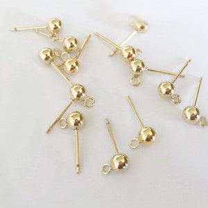 Puede incluir: Un grupo de 12 postes de pendientes de color dorado con pequeñas bolas redondas en la parte superior. Los postes están diseñados para su uso en la fabricación de joyas.