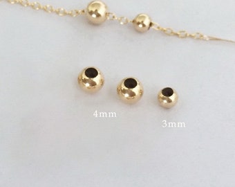 May include: Three gold-colored metal beads, one measuring 4 mm and two measuring 3 mm. The beads are round and have a smooth, polished finish.