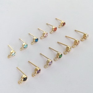 Puede incluir: Surtido de postes de pendientes de oro con pequeñas piedras preciosas de colores. Las piedras preciosas son de varios colores, incluyendo azul, verde, rojo, rosa y morado.