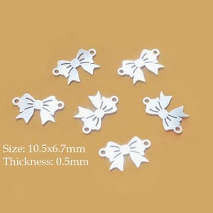 Puede incluir: Seis dijes plateados con forma de lazo con un diseño recortado, cada uno con dos pequeños bucles para sujetar. El texto indica un tamaño de 10,5x6,7mm y un grosor de 0,5mm. Ideales para la fabricación de joyas y manualidades.