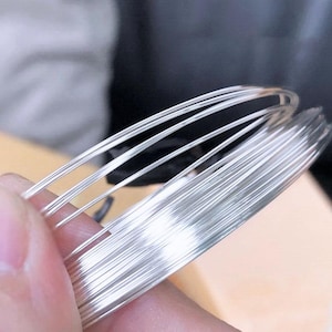 May include: A close-up of a coil of silver wire. The wire is shiny and smooth, and it is coiled tightly together.