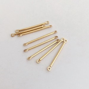 May include: A group of eight gold-colored metal jump rings with a straight bar design. The jump rings are arranged in a fan shape.