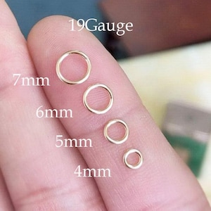 May include: Four gold-coloured open jump rings of varying sizes: 4mm, 5mm, 6mm, and 7mm. The text "19 Gauge" and measurements are visible. The rings are held between fingers.