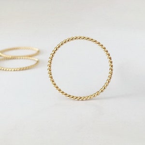 May include: A gold-coloured, twisted, thin metal ring. The ring is simple and delicate.
