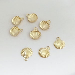 May include: Eight gold-coloured metal seashell charms with a textured surface. The charms have a loop at the top for attaching to jewellery or other crafts.