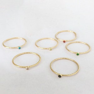 Könnte beinhalten: Sechs goldene Ringe mit kleinen farbigen Edelsteinen. Die Ringe sind dünn und haben eine strukturierte Oberfläche.