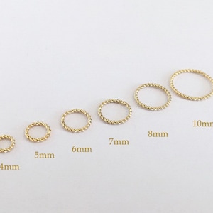 Peut inclure: Un ensemble de neuf anneaux en fil torsadé doré de différentes tailles, allant de 4 mm à 10 mm de diamètre. Les anneaux sont disposés par ordre de taille, le plus petit anneau étant à gauche et le plus grand à droite.