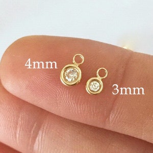 May include: Two gold charms with clear round stones. The larger charm is 4mm and the smaller charm is 3mm.