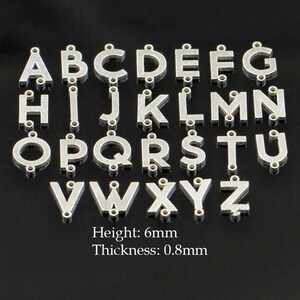 May include: Silver-colored alphabet charms, each with a loop for attaching to jewelry or crafts. The letters A through Z are displayed, with the height of each charm at 6mm and a thickness of 0.8mm.