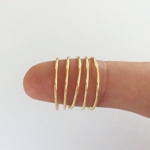 May include: Five gold stacking rings on a finger. The rings are thin and delicate.