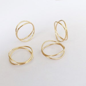 May include: Four gold-toned rings with a simple, minimalist design. Each ring features two thin bands that intersect, creating a delicate and modern look.