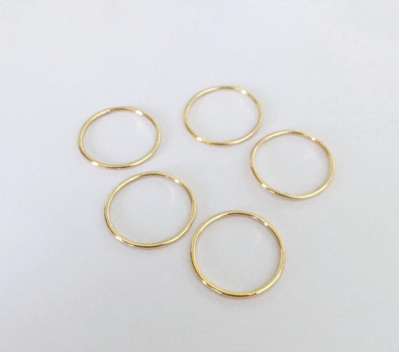 K&ouml;nnte beinhalten: F&uuml;nf d&uuml;nne, goldene Ringe liegen auf einer wei&szlig;en Oberfl&auml;che. Die Ringe sind kreisf&ouml;rmig und haben eine polierte Oberfl&auml;che. Die Ringe haben eine warme, gelbgoldene Farbe. Jeder Ring hat einen Durchmesser von etwa 2 cm.