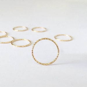 May include: A set of gold-toned, thin, twisted metal rings. The rings are arranged in a semi-circle on a white surface.