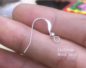 Puede incluir: Un gancho de arete plateado con un diseño curvo y una pequeña cuenta. El gancho mide 14x21mm, con una cuenta de 3mm. El gancho de arete se muestra sobre un fondo borroso.