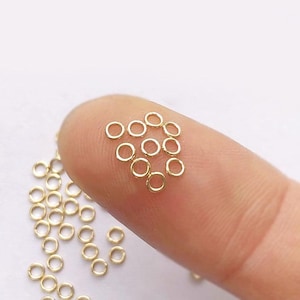 Puede incluir: Primer plano de un montón de pequeños anillos de salto dorados. Los anillos están dispuestos en un montón suelto, y algunos se superponen.