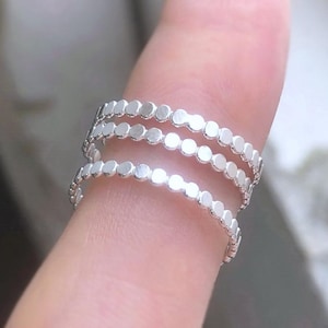 May include: Three silver rings stacked on a finger. Each ring is made of a series of small, round beads.